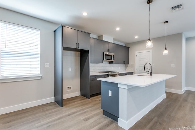 kitchen with a kitchen island with sink, hanging light fixtures, stainless steel appliances, and sink