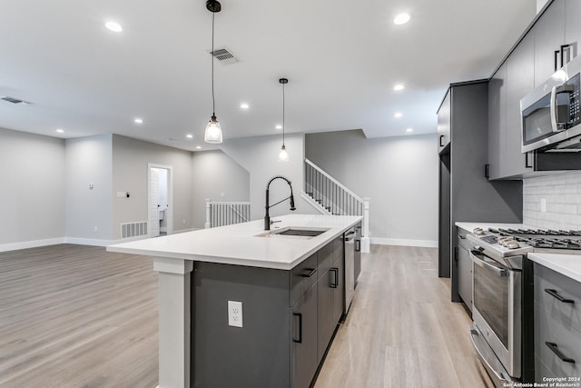 kitchen featuring decorative backsplash, appliances with stainless steel finishes, sink, pendant lighting, and a center island with sink