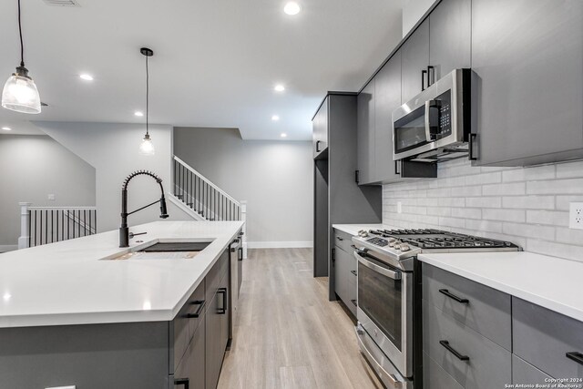 kitchen featuring gray cabinetry, sink, decorative light fixtures, appliances with stainless steel finishes, and light wood-type flooring