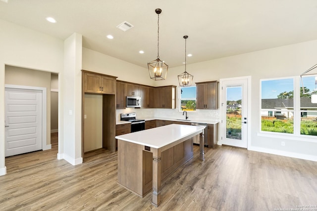 kitchen with light hardwood / wood-style flooring, a kitchen island, pendant lighting, and appliances with stainless steel finishes