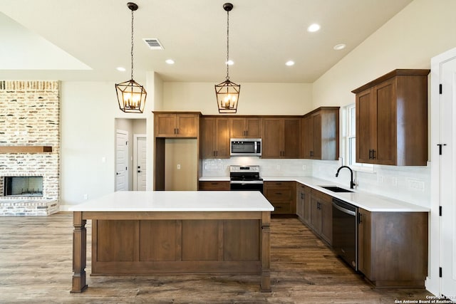 kitchen with backsplash, stainless steel appliances, sink, decorative light fixtures, and a center island