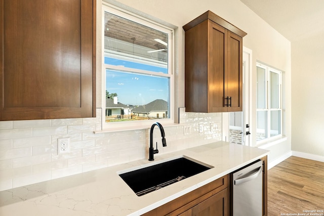 kitchen with backsplash, light stone counters, sink, and stainless steel dishwasher