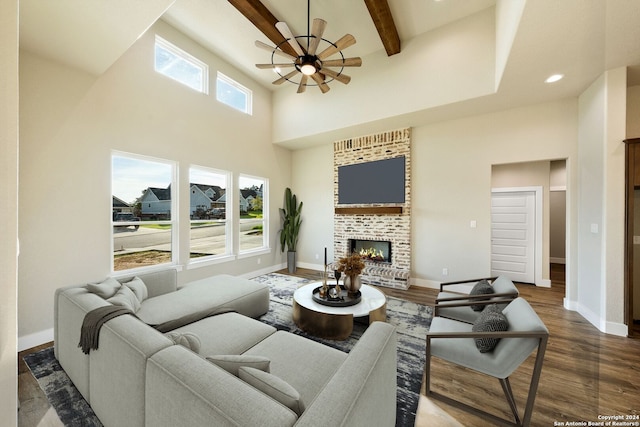 living room with dark hardwood / wood-style flooring, a towering ceiling, ceiling fan, beam ceiling, and a fireplace