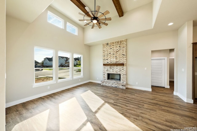 unfurnished living room featuring beam ceiling, hardwood / wood-style flooring, a brick fireplace, and ceiling fan