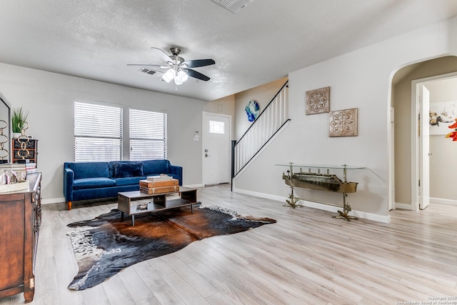 living room with ceiling fan, light wood-type flooring, and a textured ceiling