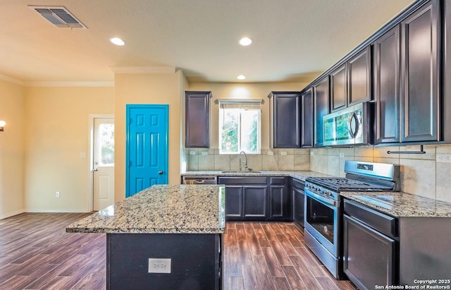 kitchen featuring a center island, sink, light stone counters, crown molding, and appliances with stainless steel finishes