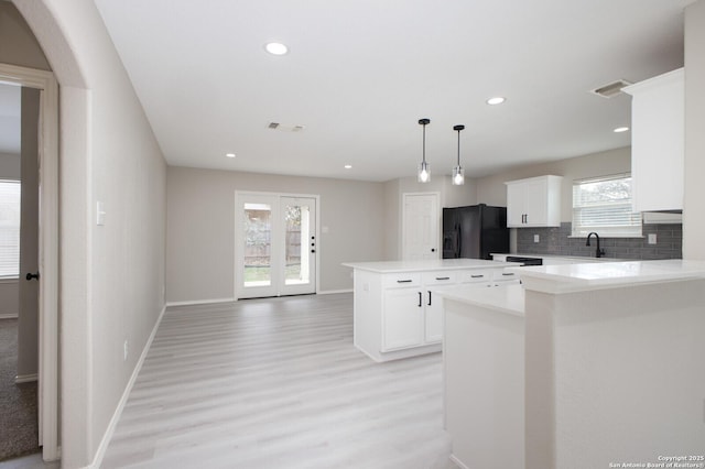 kitchen featuring decorative backsplash, black refrigerator with ice dispenser, decorative light fixtures, a center island, and white cabinetry