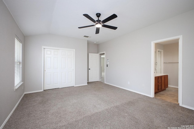 unfurnished bedroom featuring ceiling fan, ensuite bathroom, light colored carpet, lofted ceiling, and a closet