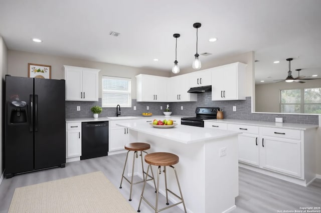 2262 Colorado Bnd, San Antonio, TX 78245 - kitchen with black appliances, under cabinet range hood, a sink, light wood-type flooring, and decorative backsplash