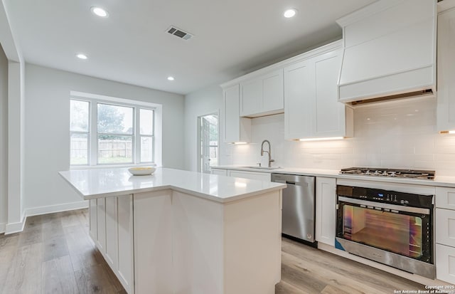 kitchen featuring appliances with stainless steel finishes, light wood-type flooring, a kitchen island, sink, and white cabinetry