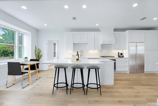 kitchen featuring custom exhaust hood, a center island, light wood-type flooring, appliances with stainless steel finishes, and white cabinetry