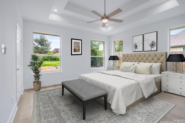 bedroom featuring light wood-type flooring, a tray ceiling, and ceiling fan