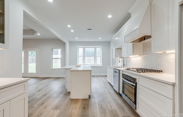 kitchen featuring appliances with stainless steel finishes, backsplash, custom exhaust hood, white cabinets, and a center island