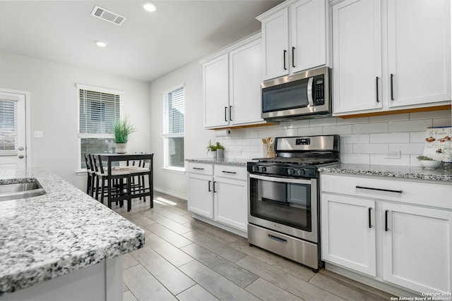 kitchen featuring backsplash, white cabinets, light wood-type flooring, appliances with stainless steel finishes, and light stone counters