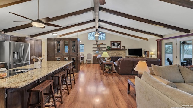 living room with a fireplace, ceiling fan, hardwood / wood-style floors, and lofted ceiling with beams