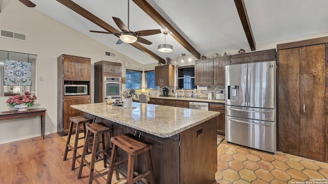 kitchen with light stone countertops, backsplash, stainless steel appliances, a center island, and a breakfast bar area