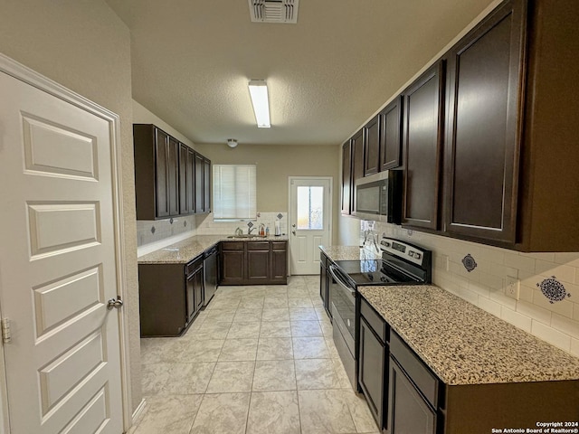 kitchen with sink, light stone countertops, a textured ceiling, appliances with stainless steel finishes, and dark brown cabinetry