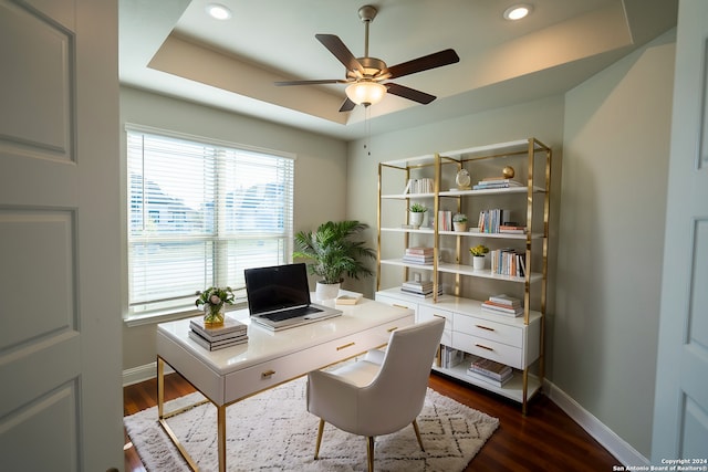 home office with dark hardwood / wood-style flooring, a tray ceiling, and ceiling fan