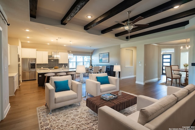 living room featuring light hardwood / wood-style flooring, beamed ceiling, ceiling fan with notable chandelier, and sink