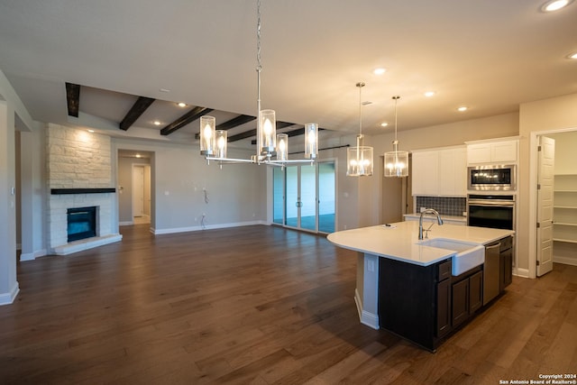 kitchen featuring pendant lighting, a center island with sink, sink, a fireplace, and appliances with stainless steel finishes