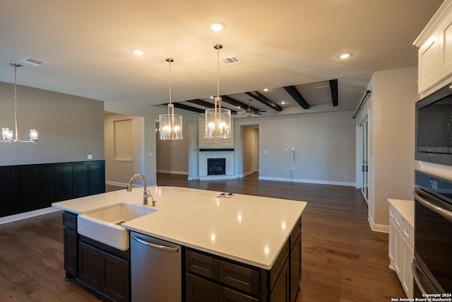 kitchen with stainless steel appliances, a kitchen island with sink, beam ceiling, a fireplace, and dark hardwood / wood-style floors