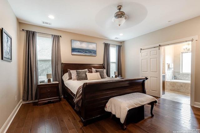 bedroom featuring hardwood / wood-style flooring, ensuite bathroom, a barn door, and ceiling fan