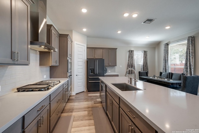 kitchen with sink, wall chimney range hood, light hardwood / wood-style flooring, decorative backsplash, and appliances with stainless steel finishes