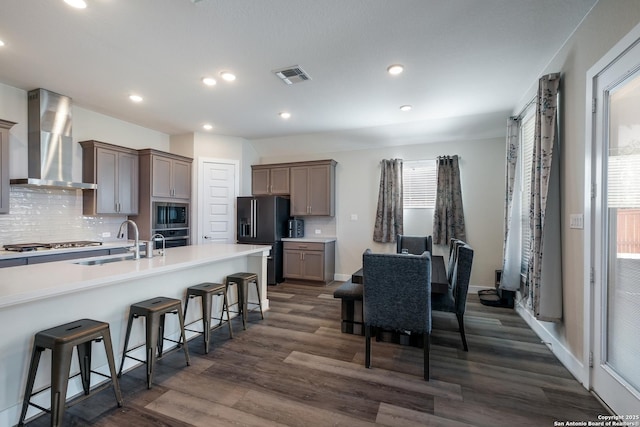 kitchen with a breakfast bar, wall chimney range hood, sink, dark hardwood / wood-style flooring, and stainless steel appliances