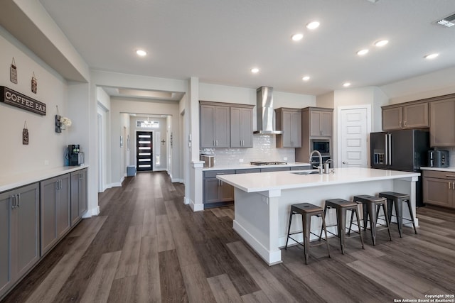 kitchen with built in microwave, wall chimney range hood, stainless steel gas cooktop, a kitchen breakfast bar, and a center island with sink