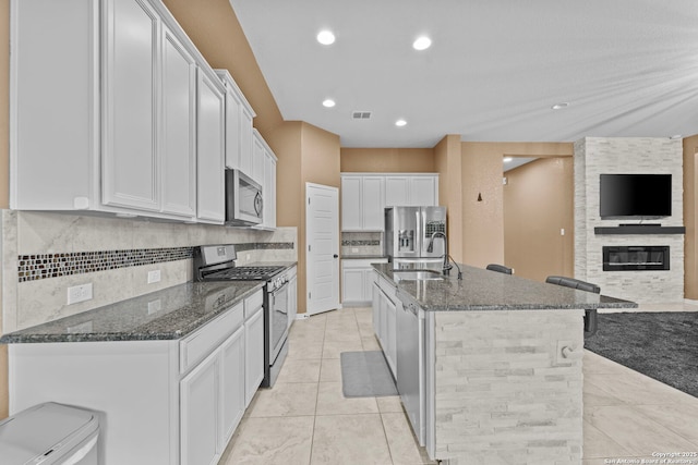 kitchen with appliances with stainless steel finishes, dark stone counters, a kitchen island with sink, sink, and white cabinetry