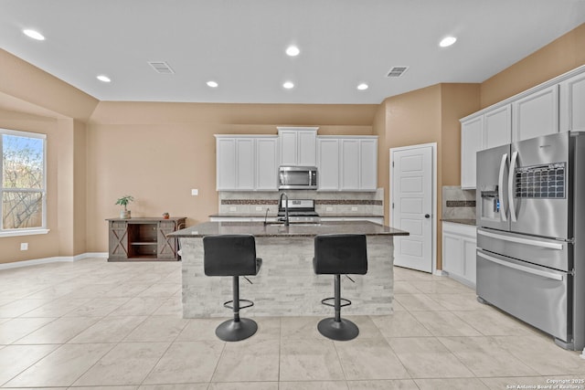 kitchen featuring a kitchen breakfast bar, white cabinetry, stainless steel appliances, and a kitchen island with sink