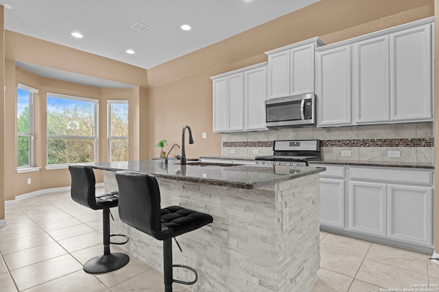 kitchen featuring sink, stainless steel appliances, dark stone countertops, a kitchen island with sink, and white cabinets