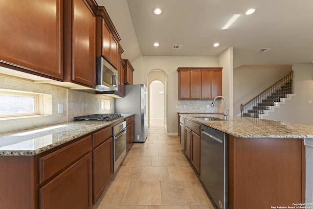 kitchen with light stone countertops, a kitchen island with sink, sink, and stainless steel appliances