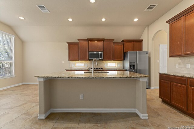 kitchen with stainless steel appliances, light stone counters, tasteful backsplash, and a center island with sink