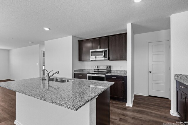 kitchen with a center island with sink, sink, light stone countertops, dark hardwood / wood-style flooring, and stainless steel appliances