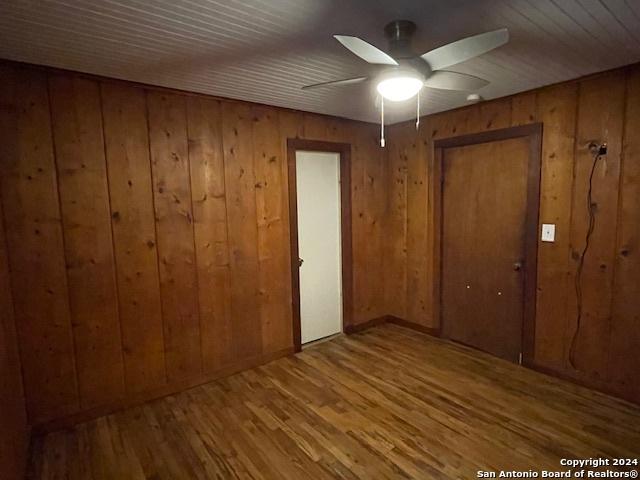 unfurnished bedroom featuring hardwood / wood-style flooring, wood walls, and ceiling fan