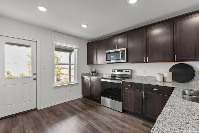 kitchen featuring light stone countertops, appliances with stainless steel finishes, dark brown cabinetry, and dark wood-type flooring