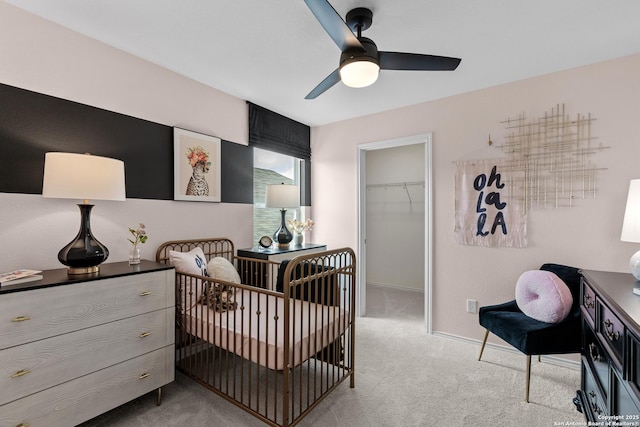 bedroom with light carpet, a walk in closet, ceiling fan, a nursery area, and a closet