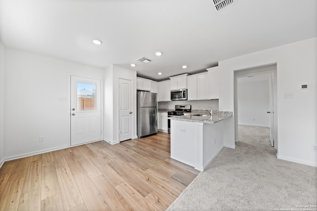 kitchen with kitchen peninsula, appliances with stainless steel finishes, light stone counters, sink, and white cabinets