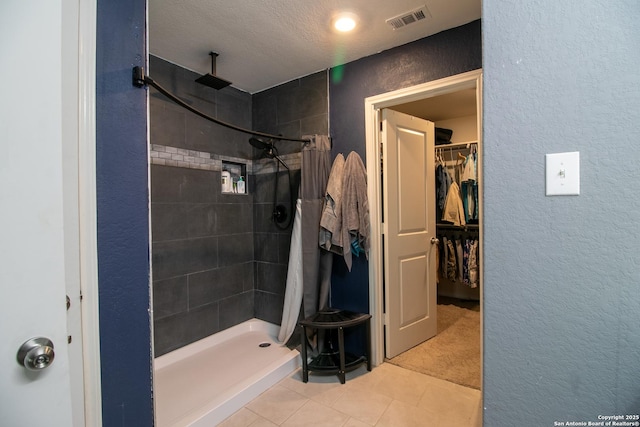 bathroom with tile patterned flooring, a textured ceiling, and tiled shower