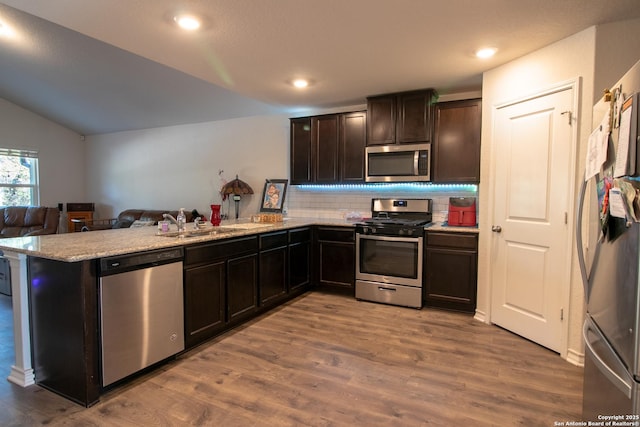 kitchen featuring decorative backsplash, wood-type flooring, kitchen peninsula, and appliances with stainless steel finishes