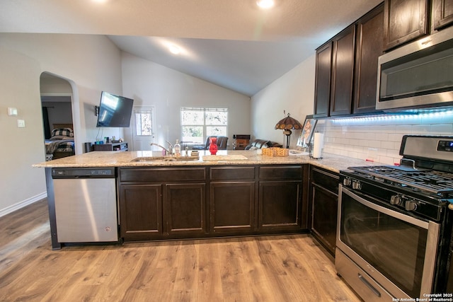 kitchen featuring kitchen peninsula, appliances with stainless steel finishes, dark brown cabinets, vaulted ceiling, and light hardwood / wood-style flooring