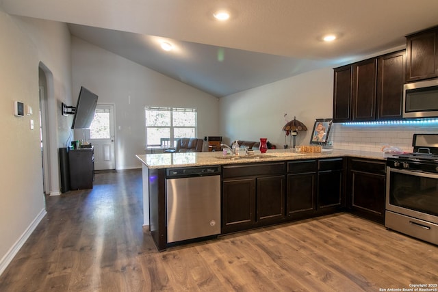 kitchen with sink, stainless steel appliances, tasteful backsplash, kitchen peninsula, and vaulted ceiling