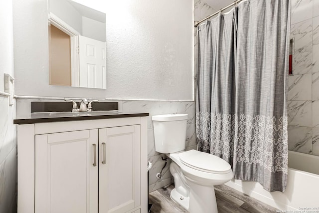 full bathroom featuring hardwood / wood-style floors, vanity, toilet, shower / bathtub combination with curtain, and tile walls