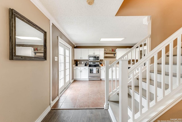 interior space with white cabinetry, a textured ceiling, appliances with stainless steel finishes, and ornamental molding