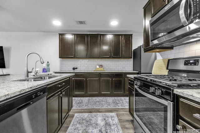 kitchen featuring sink, dark hardwood / wood-style floors, appliances with stainless steel finishes, dark brown cabinets, and light stone counters