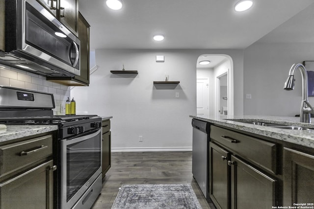 kitchen with dark wood-type flooring, sink, appliances with stainless steel finishes, dark brown cabinets, and light stone counters