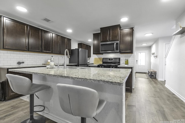 kitchen with light wood-type flooring, stainless steel appliances, a kitchen island with sink, and sink