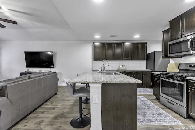 kitchen with stainless steel appliances, a kitchen island with sink, sink, light hardwood / wood-style floors, and a breakfast bar area