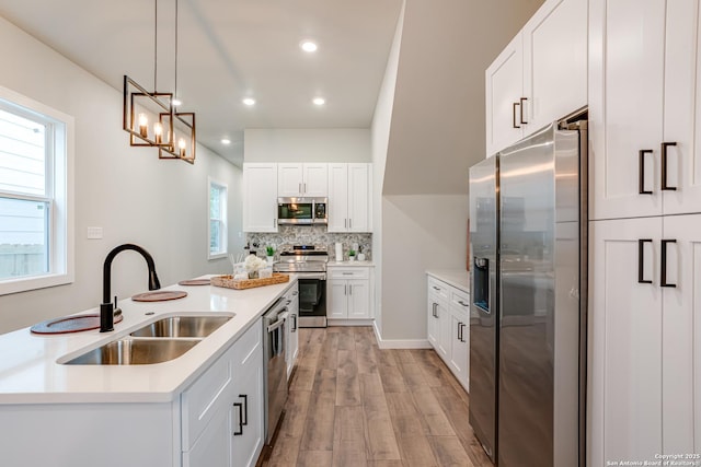 kitchen with sink, decorative backsplash, appliances with stainless steel finishes, decorative light fixtures, and white cabinetry